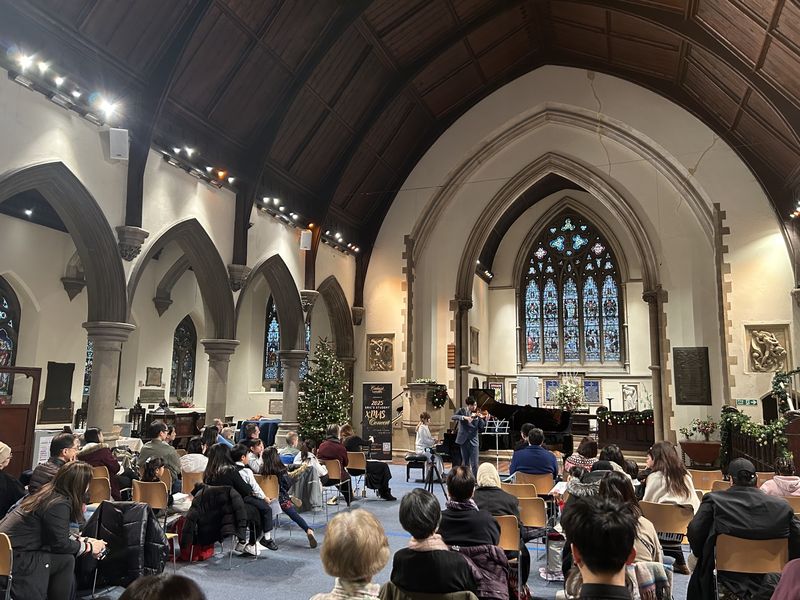 Audience of families watching Eric Chung perform violin with piano accompaniment in a church at the Christmas concert