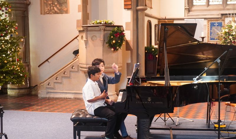Eric Chung playing a piano duet with a young student on stage during the concert