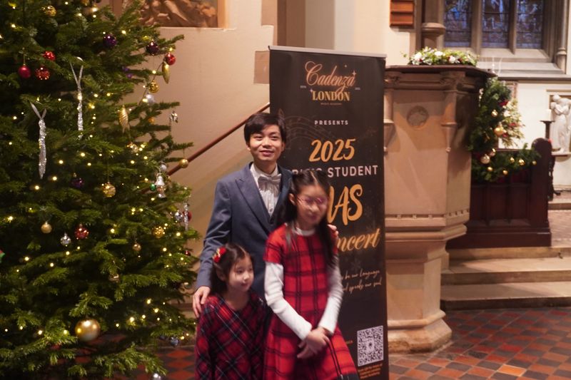 Eric Chung with two young students next to the Christmas concert banner