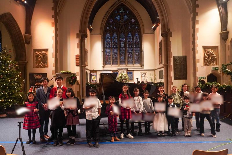Cadenza London Music Academy students holding their performance certificates in front of a Steinway grand at the 2025 Christmas concert